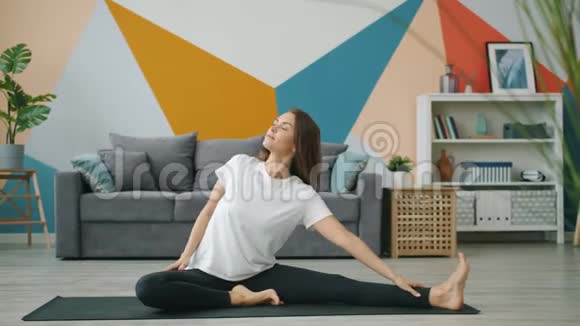 坐在公寓里的瑜伽垫上一个漂亮的女士屈着一条腿伸展身体视频的预览图