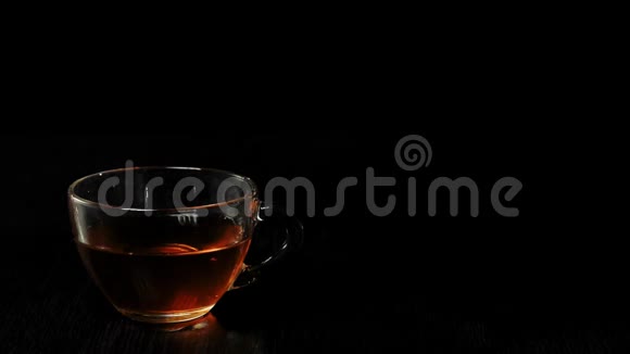 茶道红茶叶子在透明的茶壶里漂浮和旋转茶道两个冰块掉进透明的杯子里视频的预览图