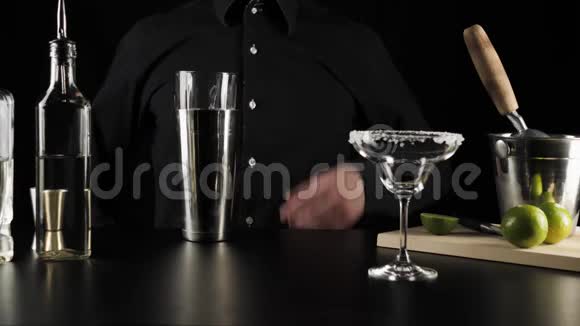 经典玛格丽塔鸡尾酒酒保拿着一个玻璃杯放在一个黑色背景的波士顿摇床上视频的预览图