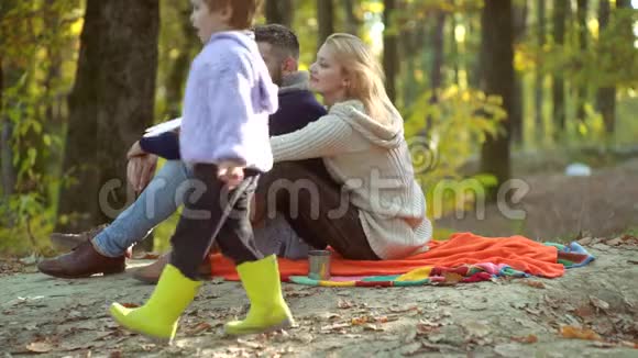 一家人坐在秋叶上浪漫和爱情微笑的夫妇和孩子的儿子走过秋天的自然视频的预览图