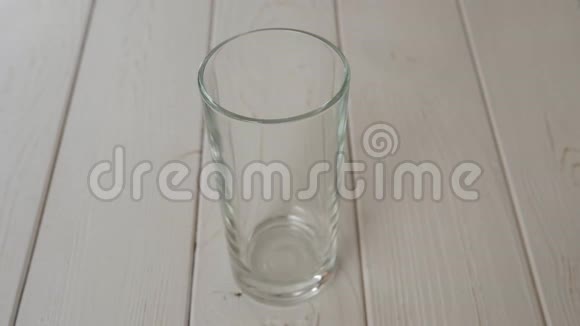 特写干净的水倒在一个玻璃上的浅色木制背景视频的预览图