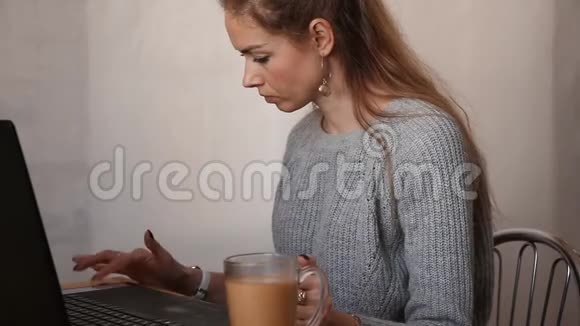 女孩坐在一张桌子上喝杯咖啡时在笔记本电脑上打字自由职业者检疫视频的预览图