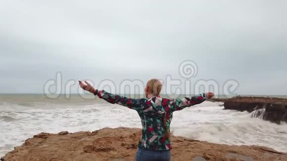 暴风雨中的海洋上美丽的女孩女孩看着远处的大海海浪在海岸上破浪前进视频的预览图