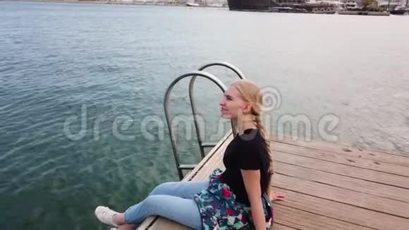 女孩独自坐在码头边的港口停靠的帆船和放松与美丽的景色视频的预览图