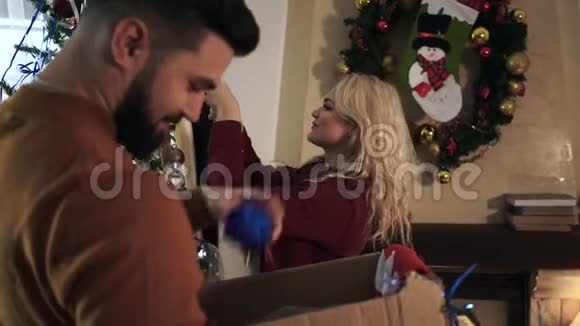 一个留着胡子的白人年轻人拿着装有圣诞装饰品的盒子和他的妻子或女朋友交谈快乐夫妻视频的预览图