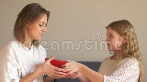 年轻可爱的女孩送给她年轻快乐的妈妈礼物盒庆祝妈妈在家坐在沙发上的母亲节视频的预览图