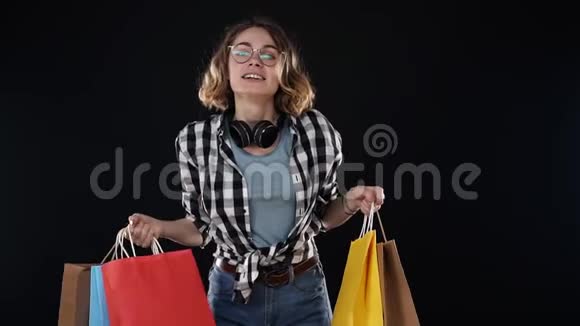 年轻的现代女性戴着耳机戴着时尚的眼镜摆着彩色纸购物视频的预览图