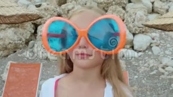 肖像快乐少年女孩戴着大太阳镜对着镜头微笑戴着蓝色大太阳镜的滑稽女孩视频的预览图
