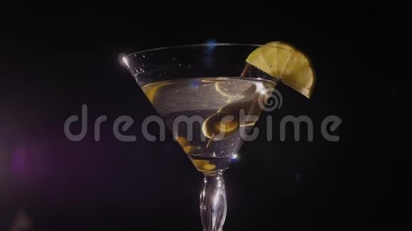 马提尼玻璃与橄榄和柠檬慢慢旋转的黑色背景视频的预览图