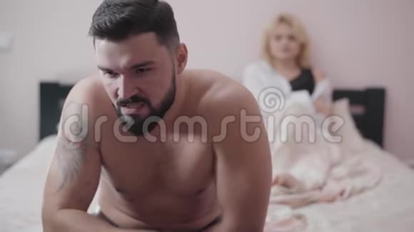 愤怒的白种人坐在床上的特写镜头模糊的金发女人躺在后台妻子欺骗丈夫视频的预览图
