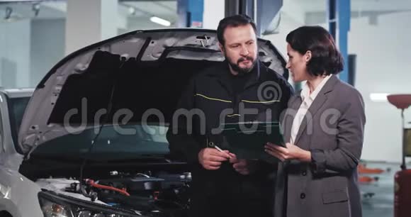 成熟的机械师和办公室经理在汽车服务中心的机械师交谈签署一些文件视频的预览图