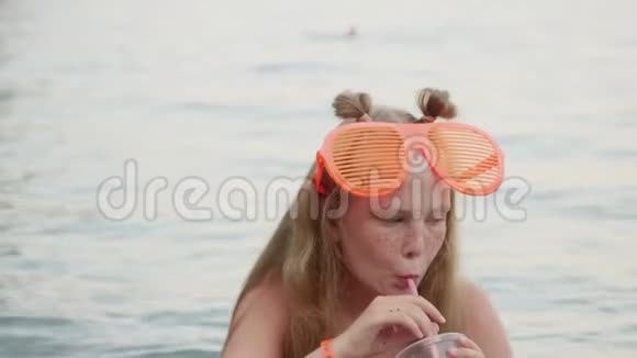 有趣的女孩青少年戴着大太阳镜喝鸡尾酒快乐的少女戴着滑稽的太阳镜放松视频的预览图