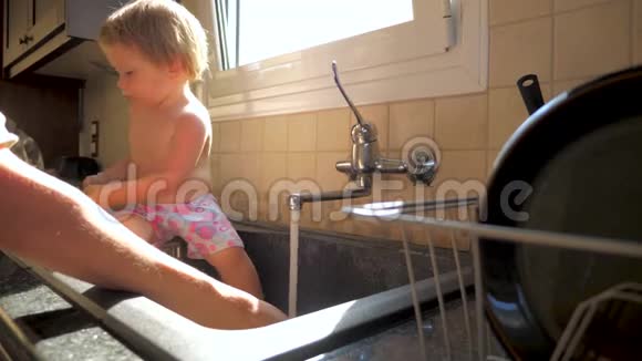 孩子坐在水槽里妈妈洗碗母女概念厨房职责家务活和视频的预览图