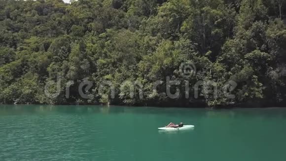 性感年轻的黑发女人躺在环礁湖中央的桨板上视频的预览图