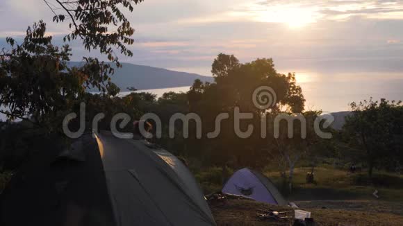 一个年轻人从露营帐篷出来在日出时站立视频的预览图