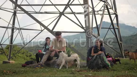 露营者坐在山上一座塔下的岩石上玩狗视频的预览图