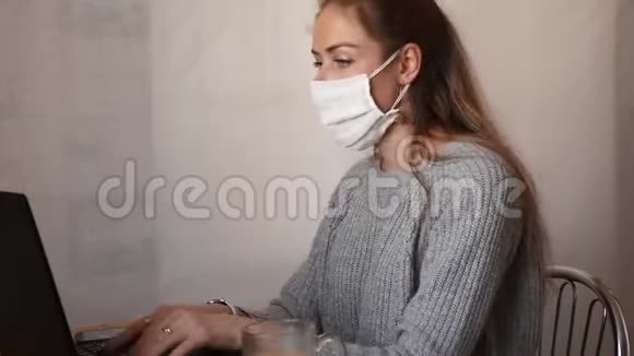 一个戴着白色防护面罩的女孩坐在桌子旁在笔记本电脑上工作在电话里交谈自由职业的概念视频的预览图