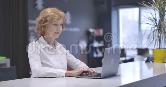 白种人中年妇女在笔记本电脑键盘上打字看着相机和微笑的肖像自信的肖像视频的预览图
