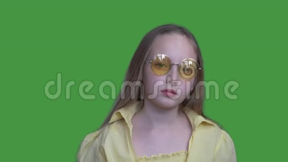 年轻的女孩十几岁戴着黄色的眼镜穿着绿色背景上的相机严肃的女孩摆着正面镜头视频的预览图