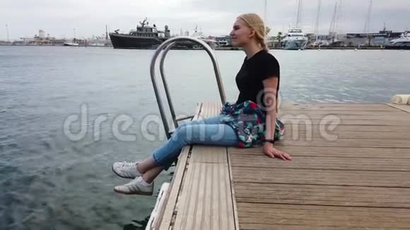 美丽的女孩坐在度假小镇港口停泊的游艇和船只的背景上视频的预览图