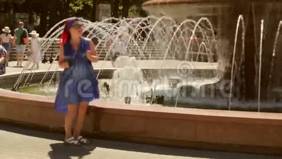 在公园的喷泉边一个穿着蓝色连衣裙的快乐的女人在跳舞视频的预览图