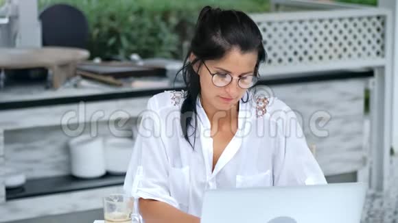 自信的自由职业者戴眼镜的女性在夏季户外咖啡馆的笔记本电脑上工作视频的预览图