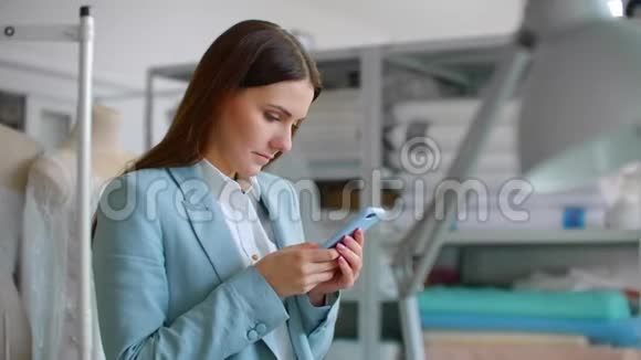 一位年轻的女设计师在缝纫车间用手机给顾客写信息与客户的沟通视频的预览图