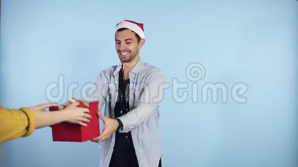 积极的年轻的男人戴着圣诞帽脖子上戴着花环从身边的女性手中得到惊喜视频的预览图