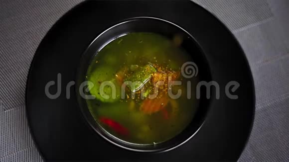 特写慢动作勺子从上到下在黑色盘子里倒入纯素汤视频的预览图