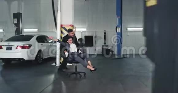 现代汽车中心服务机械师拿着一把滚动椅和他的办公室经理从服务中玩得很开心视频的预览图