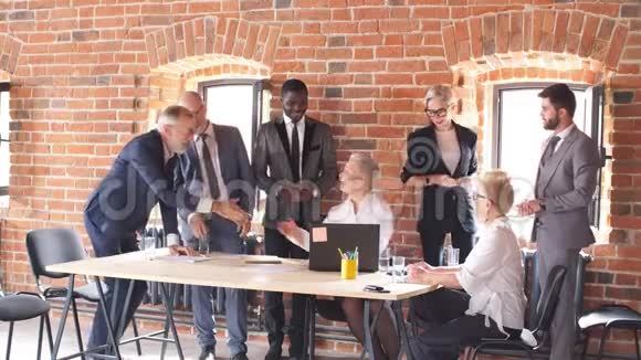 一群资深商人祝贺坐在餐桌前用笔记本电脑工作的女同事视频的预览图
