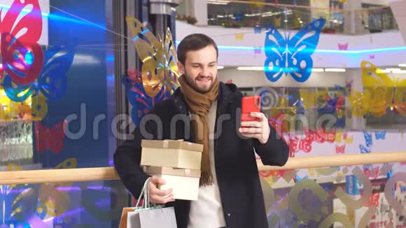 带着礼物的快乐男人在Skype上和购物中心的内部交谈视频的预览图