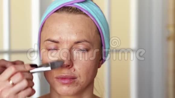 化妆师用刷子把遮瑕膏涂在女孩身上以掩盖皮肤的缺陷和痤疮手术在家里进行视频的预览图