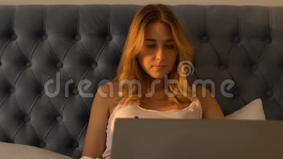 年轻女性坐在床上在笔记本电脑上看电影使用在线互联网视频的预览图