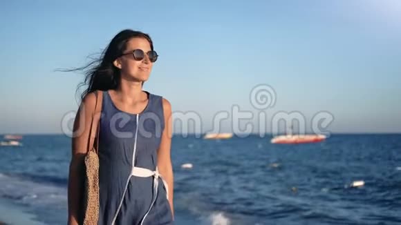 美丽的时尚女性戴墨镜日落时漫步海岸享受自由视频的预览图