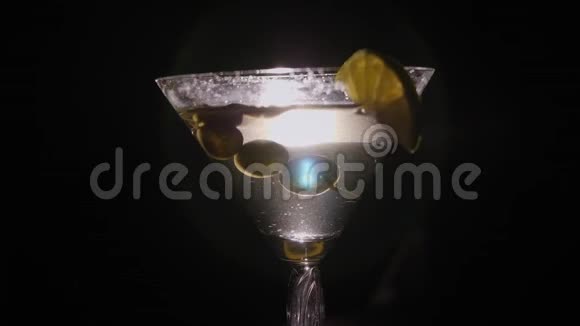 马提尼玻璃与橄榄和柠檬慢慢旋转的黑色背景视频的预览图