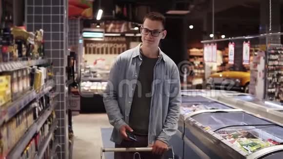 一个漂亮的年轻白种人戴着眼镜和蓝色衬衫在超市购物走在过道上视频的预览图
