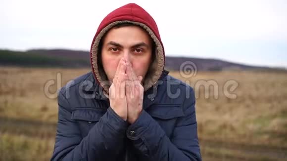 寒冷的人站在秋天的田野里试图保暖双眼紧闭将温暖的空气吹进他的手中视频的预览图