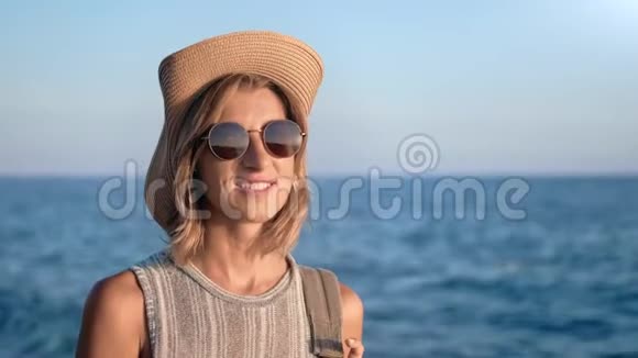带帽子墨镜背包的微笑旅游女性肖像日落背景视频的预览图