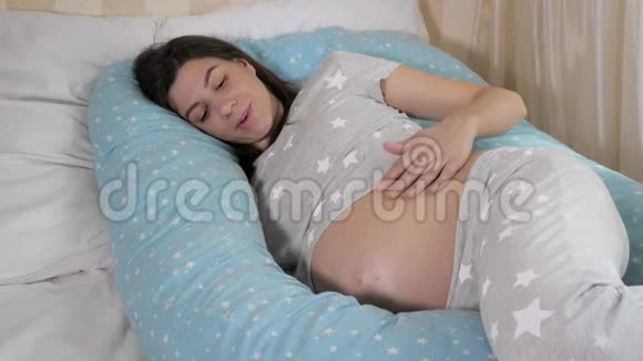 孕妇用手在床上的房间里抚摸她的胃视频的预览图