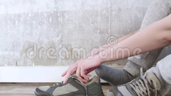 白人女孩穿着灰色裤子坐在地板上穿上运动鞋系鞋带健身用运动鞋混凝土墙面视频的预览图