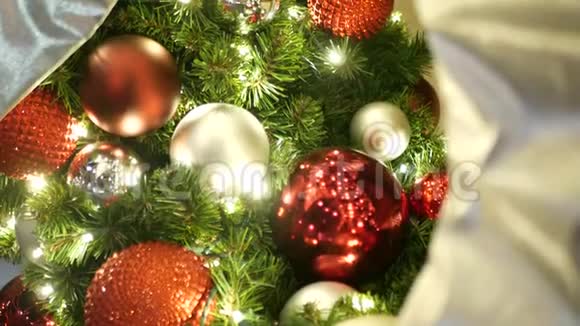 在模糊的闪闪发光的仙女背景上用鲜艳的红色球特写装饰的户外圣诞树视频的预览图