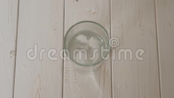 一个柠檬的特写掉进一杯水和冰在木头表面视频的预览图