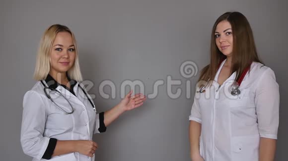 两个穿着灰色背景的白色医疗外套的女医生保健概念视频的预览图