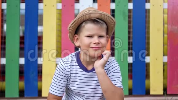 带帽子的欧洲休闲可爱男孩在操场上五颜六色的篱笆上摆姿势的肖像视频的预览图