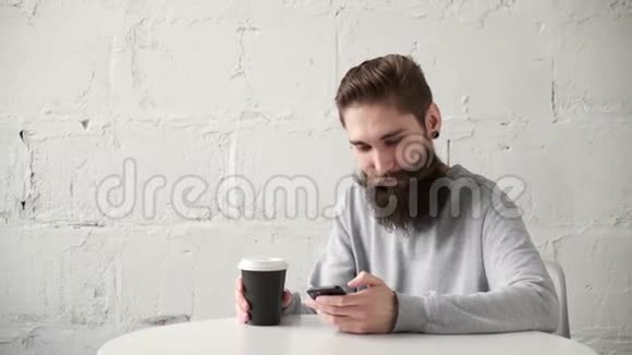 一个满脸胡子的快乐男人坐在办公桌前桌上有电话喝着咖啡视频的预览图