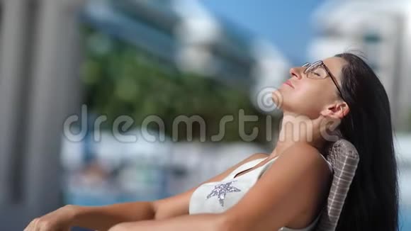 舒适的棕褐色女士戴眼镜头发在豪华的度假胜地放松日光浴中等特写镜头视频的预览图