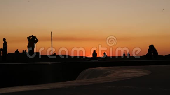 少年跳滑板的剪影骑长板夏日夕阳背景洛斯威尼斯海滨溜冰场视频的预览图