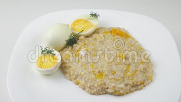 粥和两个鸡蛋用南瓜和牛奶煮大麦在白色的盘子上视频的预览图