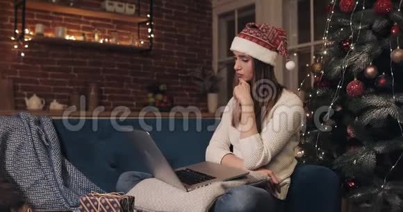 漂亮的白种人女孩坐在圣诞树附近用她的笔记本电脑思考看屏幕秩序呈现视频的预览图